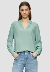 Mintgrünes Blusenshirt mit V-Ausschnitt und leichter Kragen, langen Ärmeln und weicher Textur, kombiniert mit hellblauen Jeans.