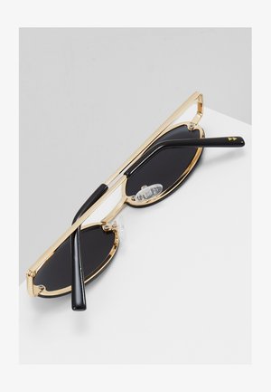 Gafas de sol con marco de metal dorado y lentes circulares negros, con patas de acetato negro y almohadillas nasales transparentes ajustables.