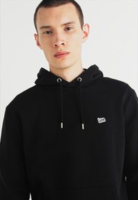 Felpa nera con cappuccio realizzata in tessuto misto cotone. Presenta un collo con coulisse, tasca a marsupio e un piccolo logo bianco sul petto.