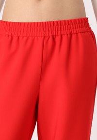 Pantalon rouge à taille élastique fabriqué dans un tissu lisse et léger. Présente une coupe décontractée sans motifs supplémentaires ni détails matériels.