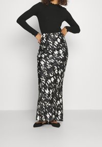 Haut noir à manches longues à côtes associé à une jupe midi noire et blanche à motifs, avec une texture lisse et une silhouette ajustée. Chaussures plates noires.