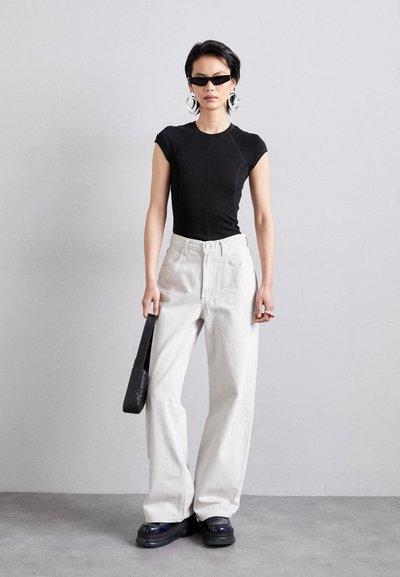Haut noir ajusté à manches courtes, jeans blancs à jambes larges, lunettes de soleil noires surdimensionnées, sac à main noir texturé, et chaussures noires chunky.