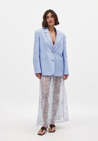 Svetlo modra blazerica z odrezanimi reverji, dvema gumboma in žepoma na nepodloženi strani, kombinirana s prosojno čipkastoc površino v beli barvi s cvetličnimi vzorci in copati.