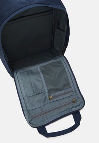 Wnętrze granatowego plecaka z szarym wykończeniem, wieloma kieszeniami, siatkową komorą i zapinanym na zamek sekcją. Posiada płaską podstawę i uchwyt na górze.