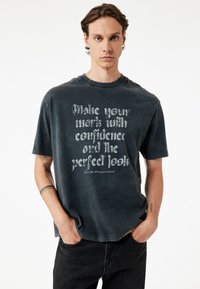 Czarnoszary, oversize t-shirt z miękkiej bawełny, z okrągłym dekoltem, z wyraźnym białym napisem i krótkimi rękawami. Luźny krój o minimalistycznym designie.