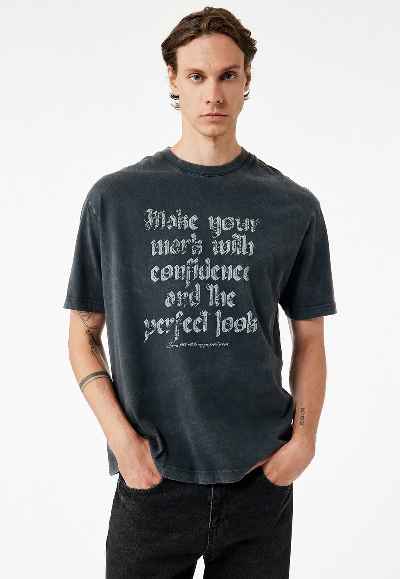 Czarnoszary, oversize t-shirt z miękkiej bawełny, z okrągłym dekoltem, z wyraźnym białym napisem i krótkimi rękawami. Luźny krój o minimalistycznym designie.