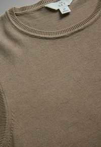 Suéter beige con cuello redondo, collar acanalado y textura suave. Etiqueta visible: "THE SET", talla M, con detalles de cuidado del tejido.