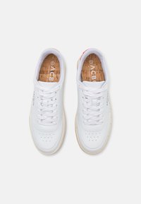 White leather sneakers with a smooth surface, lace-up front, perforated toe, and cork insoles, featuring red accents on the heel.