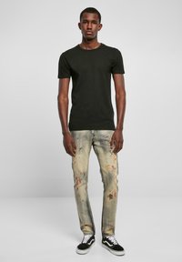 Svart bomulls T-skjorte med rund hals, sammen med slitte lyse jeans med malingsplatter og svarte sneakers med hvite detaljer.