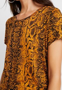 Pomarańczowa bluzka z krótkim rękawem w czarny wzór w węża. Wykonana z teksturowanej tkaniny, z okrągłym dekoltem i luźnym krojem.