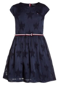 Robe marine avec un corsage ajusté, des manches courtes, des motifs d'étoiles et une jupe plissée. Comprend une ceinture rayée blanche et rouge pour l'accentuation.