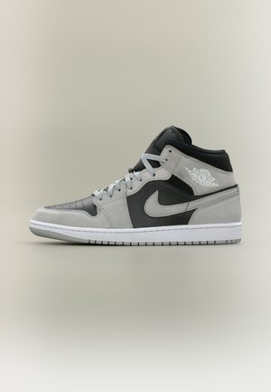 Air Jordan 1 mid-top tenisica od crnog i sivog brušenog kože s bijelim Nike logotipom i gumenim potplatom, prikazana sa bočnog profila na neutralnoj pozadini.