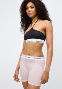 Μαύρο αθλητικό σουτιέν με έναν ώμο και λευκό λογότυπο Calvin Klein. Ανοιχτό ροζ μπόισορτς με αντίστοιχο ελαστικό λογότυπο στη μέση.