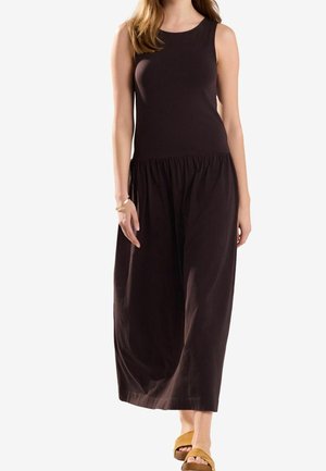 Sleeveless maxi dress in dark brown, featuring a fitted bodice and loose, gathered skirt. Made of smooth fabric; worn with tan sandals.