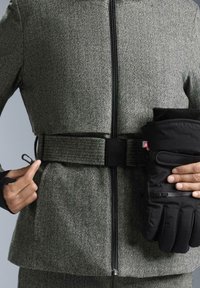 Sivý sako v herringbone vzore s čiernym panelovým opaskom, so zipsom a bočnými vreckami. Čierne rukavice so zipsom na rukách.