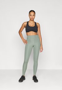 Sujetador deportivo negro y leggings de tiro alto en verde menta con textura suave y costuras en contraste, combinados con zapatillas deportivas negras.