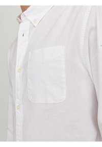 Camisa blanca de botón, fabricada con tejido texturizado, que cuenta con un bolsillo en el pecho y botones amarillos, con un cuello clásico y un corte ajustado.