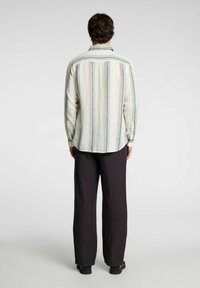 Camicia a righe da uomo con linee orizzontali multicolori su uno sfondo chiaro, dotata di colletto e polsini кнопa, abbinata a pantaloni scuri.