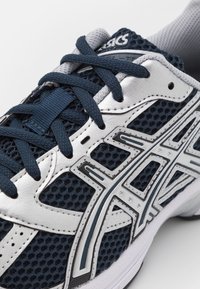 Laivastonsininen ja valkoinen ASICS-juoksukenkä, jossa on hengittävä verkko, paksut nauhat ja erottuva hopeinen ASICS-logo sivulla.
