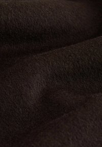 Gros plan sur un tissu en laine douce de couleur brun foncé avec une texture visible et des plis délicats mettant en valeur sa surface pelucheuse et moelleuse.