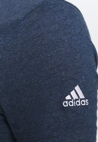 Granatowa koszula z krótkim rękawem, wykonana z teksturowanej tkaniny, z białym logo Adidas na lewym ramieniu.