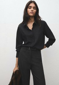 Czarna koszula na guziki z długimi rękawami, zestawiona z ciemnoszarymi, dopasowanymi spodniami. Gładka tkanina z subtelnym połyskiem, charakteryzująca się minimalistycznym wzornictwem.