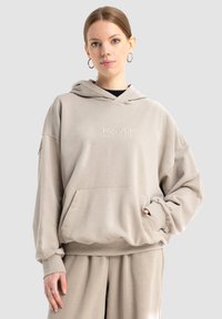 Beżowa, oversize bluza z kapturem, z kieszenią z przodu, regulowanym kapturem i haftowanym logo "DROUGHT". Miękki materiał o gładkiej fakturze.