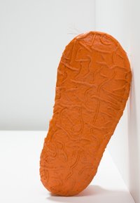 Orange gummisula med strukturerad yta och vågiga mönster, som avsmalnar mot tån. Kanten är något oregelbunden och tjock.