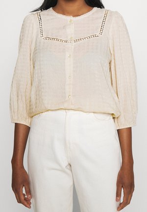 Blusa color crema in tessuto texture, con collo rotondo, chiusura con bottoni e dettagli in crochet su spalle e maniche.