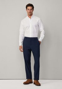 Chemise blanche à boutons, pantalon marine, chaussures marron. Coupé droit, tissu lisse, col discret et poches avant sur le pantalon.