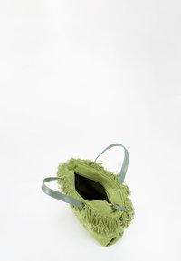 Borsa di stoffa verde con dettagli frangianti intorno alla parte superiore, due manici azzurri chiari e chiusura con zip. L'interno è foderato e spazioso.