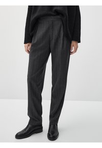 Pantaloni grigi a righe con un fit rilassato e frontale plissettato. Realizzati in tessuto strutturato, abbinati a stivaletti neri in pelle.