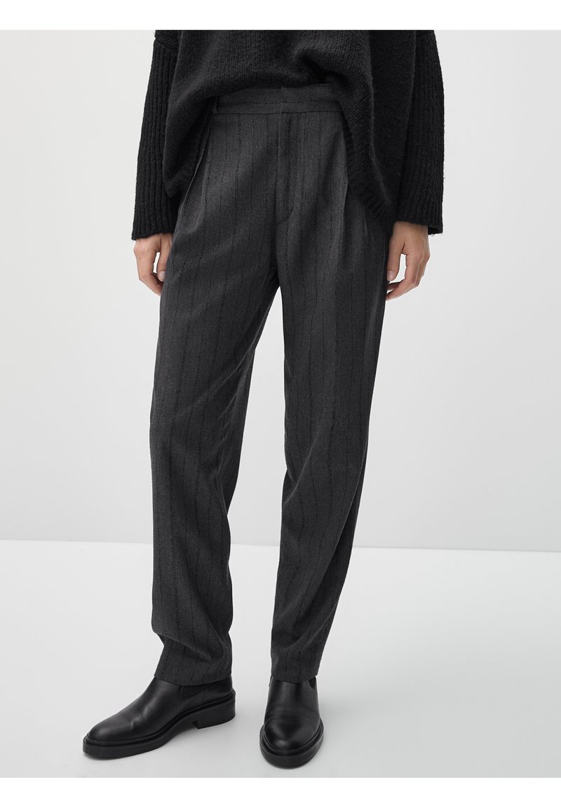 Pantaloni grigi a righe con un fit rilassato e frontale plissettato. Realizzati in tessuto strutturato, abbinati a stivaletti neri in pelle.