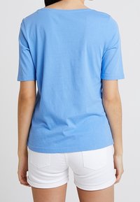 Vaaleansininen puuvillainen T-paita, jossa on lyhyet hihat ja pyöreä pääntie, yhdistettynä valkoisiin shortseihin, joissa on piilotetut takataskut.