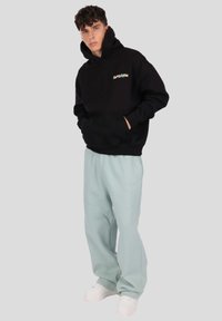 Fekete kapucnis pulóver kis, színes grafikával a mellkason, világos menta színű melegítőnadrággal és fehér sportcipővel párosítva.