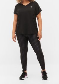 T-shirt nera a collo a V con maniche corte, abbinata a leggings neri con un motivo di testo ripetuto. L'outfit è completato da scarpe sportive.