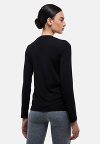 T-shirt noir à manches longues en tissu doux, avec un col rond et une coupe ajustée, associé à des leggings gris texturés.
