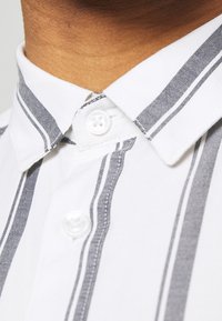 Button-up shirt with white fabric and narrow gray vertical stripes. Features a classic collar and two buttons at the collar.