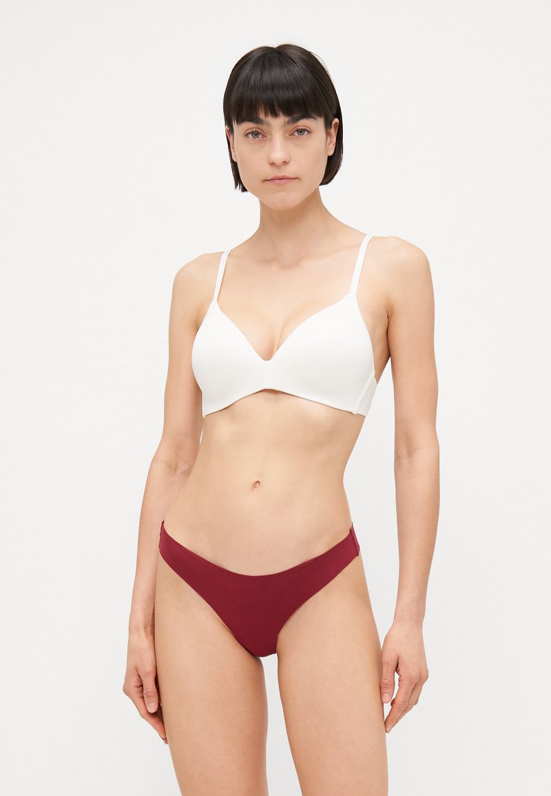 Vit plunge-bh med justerbara band och slät yta, i kombination med bordeauxfärgade bikiniunderbyxor med låg midja, som har en enkel design.