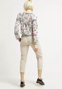 Blus med blommönster och elastiska ärmmuddar samt nederkant i lätt tyg; matchad med figurnära beige byxor och svarta snörskor.