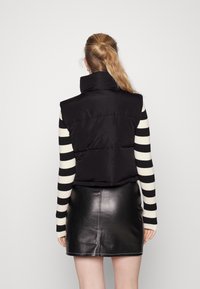 Czarna kurtka puchowa z wysokim kołnierzem, pikowanym wzorem i skróconym krojem, noszona na czarno-białym swetrze w paski oraz skórnej spódnicy.