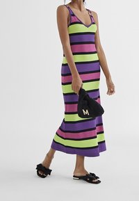 Randig maxiklänning i grönt, lila och rosa med svarta detaljer. Har en v-ringning, tunna axelband och vertikala ränder; matchas med en svart kuvertväska.