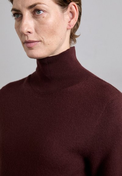 Burgundin turtleneck villapaita, ribbaatukaalinen kaula-aukko, pehmeä tekstuuri, vartalonmyötäinen muotoilu ja minimaalinen saumuros. Normaali leikkaus vyötäröllä.