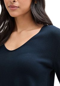 Haut en tricot bleu marine avec un décolleté large et arrondi, ajusté au corps. Le matériau semble doux avec une finition texturée.