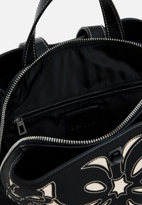 Schwarze Handtasche mit texturierter Oberfläche, die ein kontrastierendes Blumendesign aufweist. Das Innere verfügt über ein Reißverschlussfach und eine glatte Fütterung, die mit einem Reißverschluss gesichert ist.