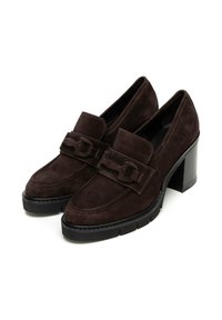 Mocassins en daim marron à talons avec une semelle noire épaise, présentant une sangle en cuir décorative avec un détail de boucle à l'avant.