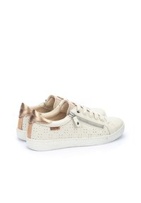 Zapatillas de cuero color crema con diseño perforado, acentos de talón en oro texturizado, cordones delanteros y detalle de cremallera lateral. Suela de goma.