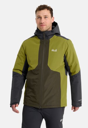 Man die een groene en donkergrijze waterdichte jas met capuchon draagt, staat en kijkt iets omhoog naar rechts.