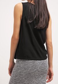 Haut noir sans manches à coupe décontractée, associé à une jupe grise mouchetée. Le haut présente une texture lisse et un ourlet arrondi.