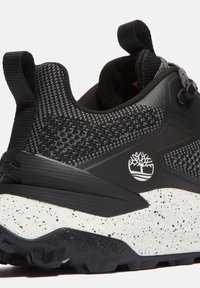 Svart och grå atletisk sko med ett texturerat mesh-övre, en förstärkt häl och en fläckig vit mellansula. Har en logo på sidan.